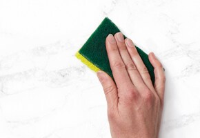 Hand wiping marble benchtop with Scotch-Brite sponge